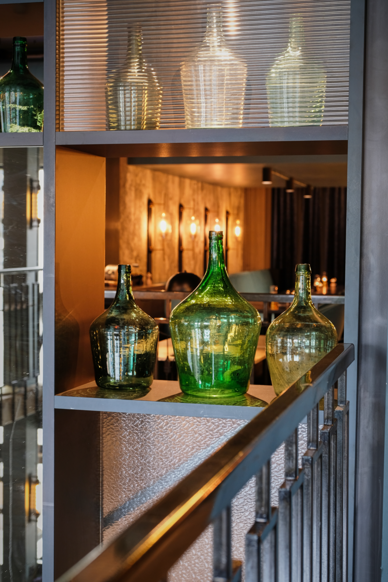 Groene glazen flessen als decoratie in het interieur van restaurant Octave